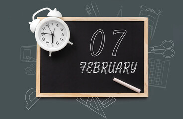 february 7. 7th day of month, calendar date.   Blackboard with piece of chalk and white alarm clock on green background. Concept of day of year, time planner, winter month