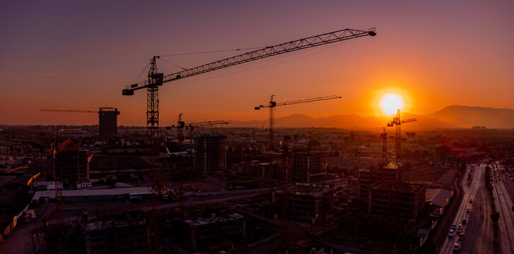 Gr&uacute;as giratorias o gr&uacute;as pluma operan y trabajan en la industria de la construcci&oacute;n de edificios residenciales y de oficinas en Santiago de Chile con una c&aacute;lida puesta de sol. Progreso, crecimiento.