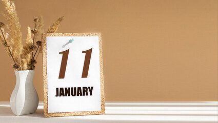 january 11. 11th day of month, calendar date.White vase with dead wood next to cork board with numbers. White-beige background with striped shadow. Concept of day of year, time planner, winter month