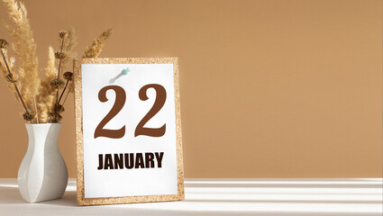 january 22. 22th day of month, calendar date.White vase with dead wood next to cork board with numbers. White-beige background with striped shadow. Concept of day of year, time planner, winter month