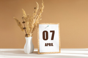 April 7. 7th day of month, calendar date.White vase with dried flowers on desktop in rays of...