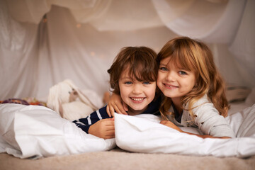 Siblings make the best of friends. Shot of two adorable siblings lying in their blanket fort indoors. - obrazy, fototapety, plakaty