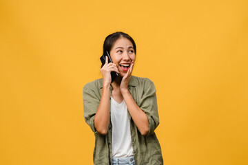 Young Asia lady talk by phone with positive expression, smile broadly, dressed in casual clothing feeling happiness and stand isolated on yellow background. Happy adorable glad woman rejoices success.