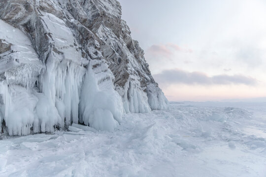 A beautiful cliff surrounded by frozen ice and hummocks seen on frozen winter lake Baikal with mountainous background during sunset. Art photo landscape, winter landscape