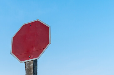 rusty old stop sign on concrete pole against blue sky background