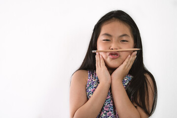 Isolated portrait of Asian little girl on white background, positive feeling little girl, funny pose by balancing a pencil between her mouth and nose, black long hair. Concept for children education.