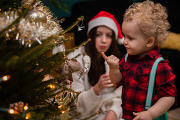 A little boy is wondering how to hang an ornament on his Christmas tree.