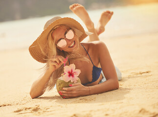 Sipping on something tropical. Portrait of a happy young woman in a bikini enjoying a cocktail while lying on the beach.