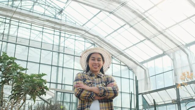 Happy gardener woman standing with her arms crossed and looking at the camera in the greenhouse.