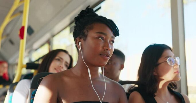 A young beautiful woman with a dark complexion rides a bus on a summer afternoon, a girl with dreadlocks tied up in a bun has headphones in her ears, listens to music, hums songs.