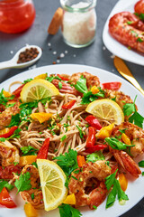Stir fry noodle with shrimps, lemon and fresh parsley on white plate, soba with prawns, asian cuisine, top view