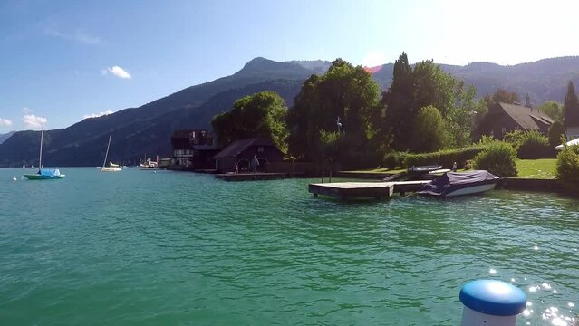 beautiful lake in austria called wolfgangssee with mountains, smooth water, a jetty with sailing boat near by a little village with a boat hut -a sunny day with a blue sky all in all a nice summeday