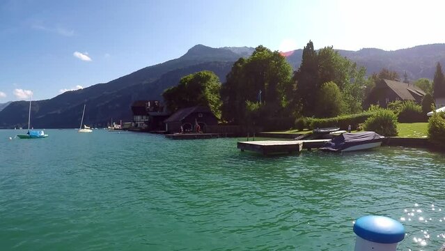 beautiful lake in austria called wolfgangssee with mountains, smooth water, picnic guys a jetty with sailing boat near by a little village with a boat hut -a sunny day with a blue sky