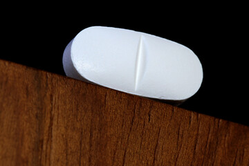 A paracetamol or ibuprofen pill photographed at high magnification on the corner of a table