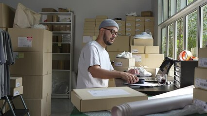 Asian man online seller confirming orders from customer on the phone. E-commerce business owner looking at the phone in store warehouse.