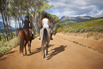 Going for a ride. Rear-view of two women on horseback - riding trail.