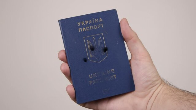 Holes in shot Ukrainian passport. Concept of occupation of the country, the war in Ukraine. Male hand holding a blue document. Russian aggression, occupiers