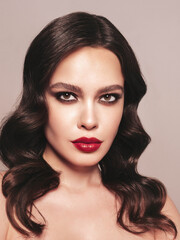 Beauty portrait of young brunette woman with evening makeup and perfect clean skin. Sexy model with curly hair posing in studio near dark wall. With red bright natural lips. In silver dress