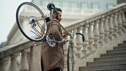 Young stylish man carrying his bicycle upstairs, retro bike in sunny day. - Powered by Adobe