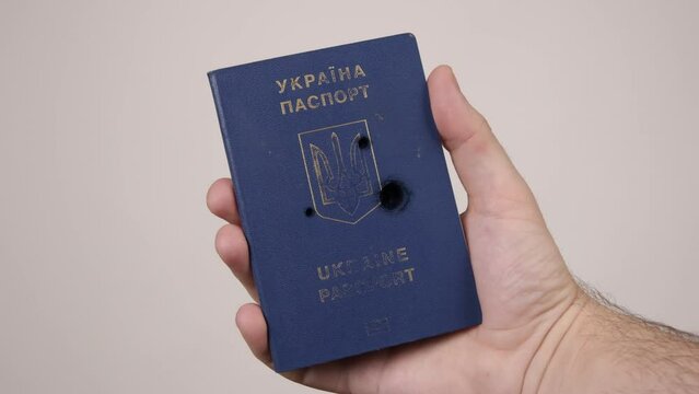 Man's hand holds a passport of Ukraine shot with bullets. Concept of war in Russia against Ukraine. Aggression of occupiers, genocide of the people