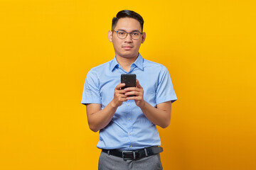 Pensive young asian man Asian in glasses reply to incoming messages on mobile Phone isolated on yellow background. businessman and entrepreneur concept