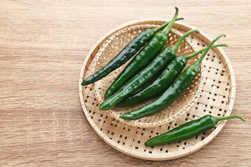 Green chili served in bamboo plate on wooden table.
