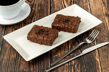Chocolate covered raisin cake on wooden table with filter coffee