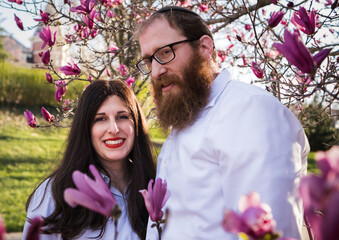 Outdoor, portrait of middle aged Jewish couple by blooming magnolia tree in spring 