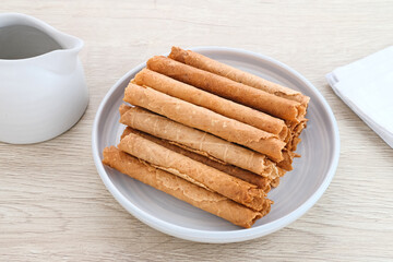 Waffle egg rolls or semprong cake, a traditional Indonesian snack with a unique shape like a layered pipe, served on a white plate. Selected focus.

