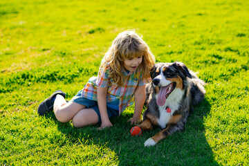 Little blond boy with her pet dog outdooors in park. Child with pet puppy dog. A child with a dog playing in nature on green grass.