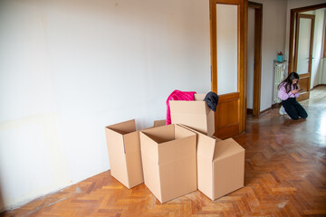 Moving to a new home concept. Cardboard boxes along the  parquet floor of a empty room with a young girl seated on the background.