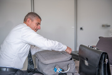 Businessman packs his suitcase for a business trip. Briefcase and clothes on the bed.