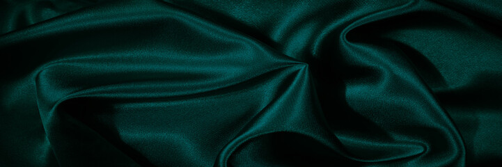 Dark green silk satin. Shiny silky surface of the fabric. Wavy folds. Elegant background with space...