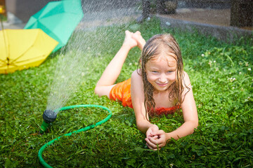 Child playing with garden sprinkler. Summer outdoor water fun in backyard. Ggirl play with hose watering grass. Kid splash on hot sunny day