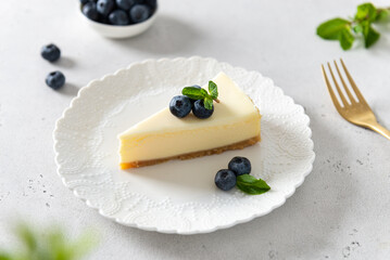 New York cheesecake or classic vanilla cheesecake with fresh blueberries and mint on white stone background. Side view, close up. Menu, recipe, confectionery