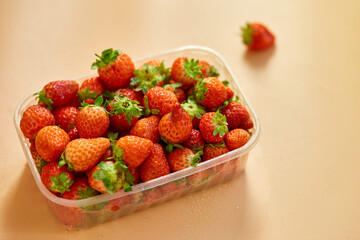 Red ripe organic strawberries in plastic tray container on orange background, copy space for text, top view, market local farm concept, harvest.