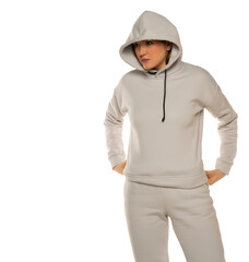 a young woman in a gray tracksuit and hood poses against a white background in the studio