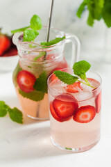 Homemade refreshing strawberry lemonade in glass and jug with fresh strawberries and mint leaves. Summer drink 