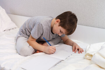 The child draws with a pencil on paper while sitting on the bed, close-up. Hobby - 496759653