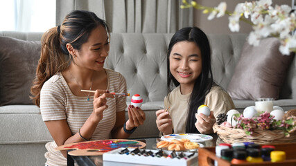 Asian young mother and daughter painting eggs preparing for Easter celebration. Easter, holidays and people concept.