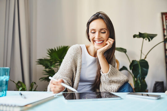 Happy woman using digital tablet with digitized pen sitting at desk