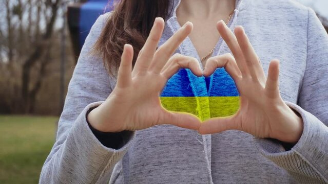 Unrecognizable woman folded her arms in shape of heart with flag of Ukraine protesting against war. Crisis, peace, stop aggression in whole world