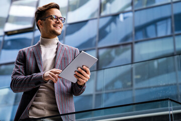 Happy young business man with tablet at work in modern urban background