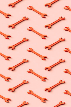 Three dimensional pattern of rows of orange colored wrenches flat laid against beige background