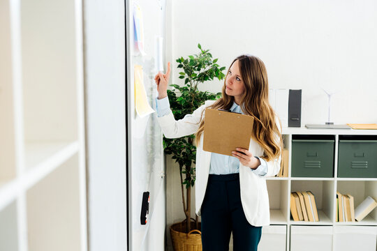 Businesswoman holding file folder examining chart on whiteboard in office