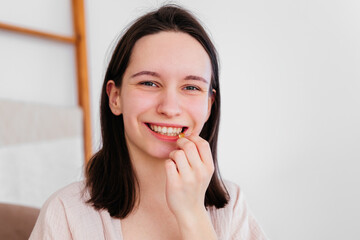 Smiling young woman holding pill omega capsule in hand looking at camera indoors. Girl taking...