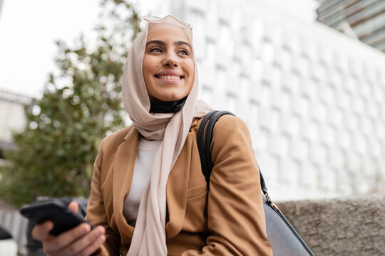 Smiling young businesswoman with mobile phone at office park