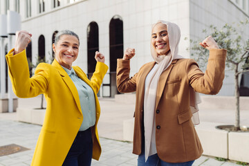 Happy businesswomen flexing muscles standing at office park on sunny day