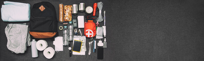 Emergency backpack equipment organized on the table. Documents, water,food, first aid kit and another items needed to survive.