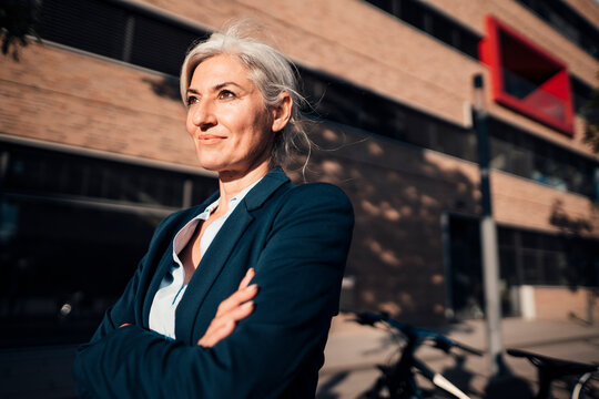 Confident businesswoman standing with arms crossed at office park on sunny day
